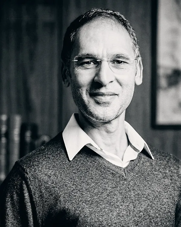 Christophe Fassi, photographe, en pull gris et chemise blanche, sourire discret, noir et blanc.